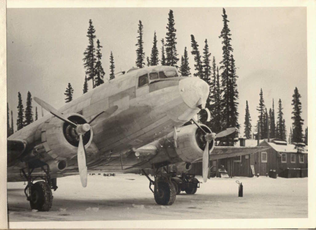 Aircraft parked with snow on the ground and pine trees in the background